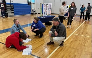 Doug Ware, ELO Coordinator at Mt. Ararat engages with a student working on their financial fitness packet. Around them credit union representatives talk with students about financial literacy.