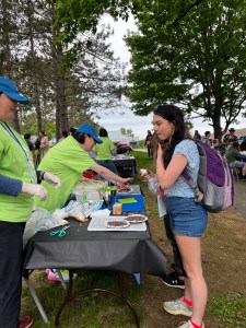 A young woman wearing a blue top and shorts speaks to two women in bright green shirts.