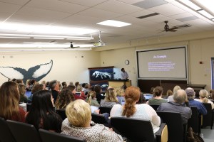 presenter talking to a room full of educators with projector displaying text.