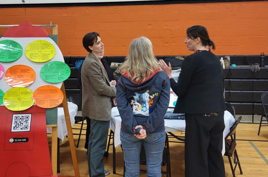 Teachers talking to each other standing by a display.