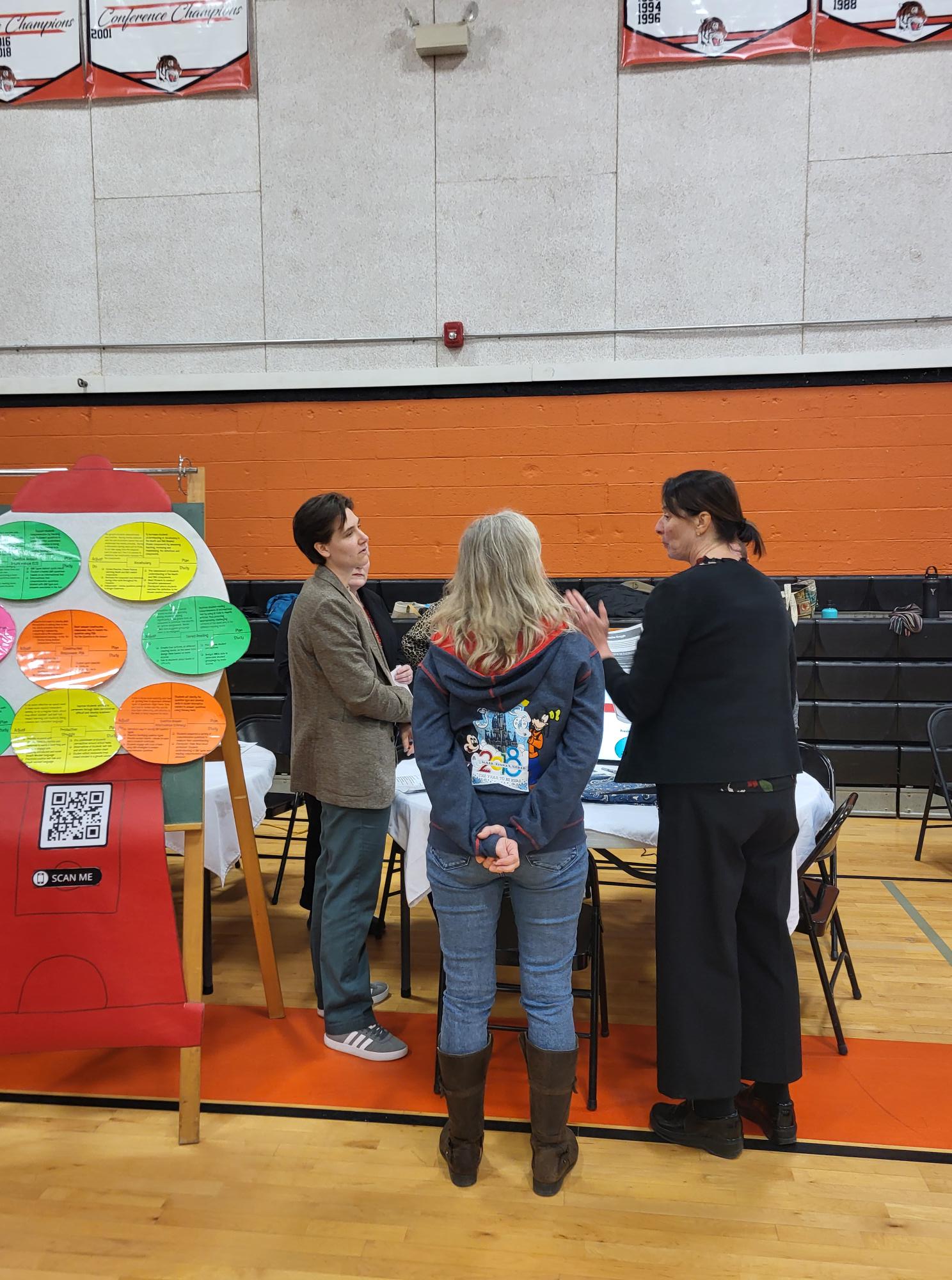 Teachers talking to each other standing by a display.
