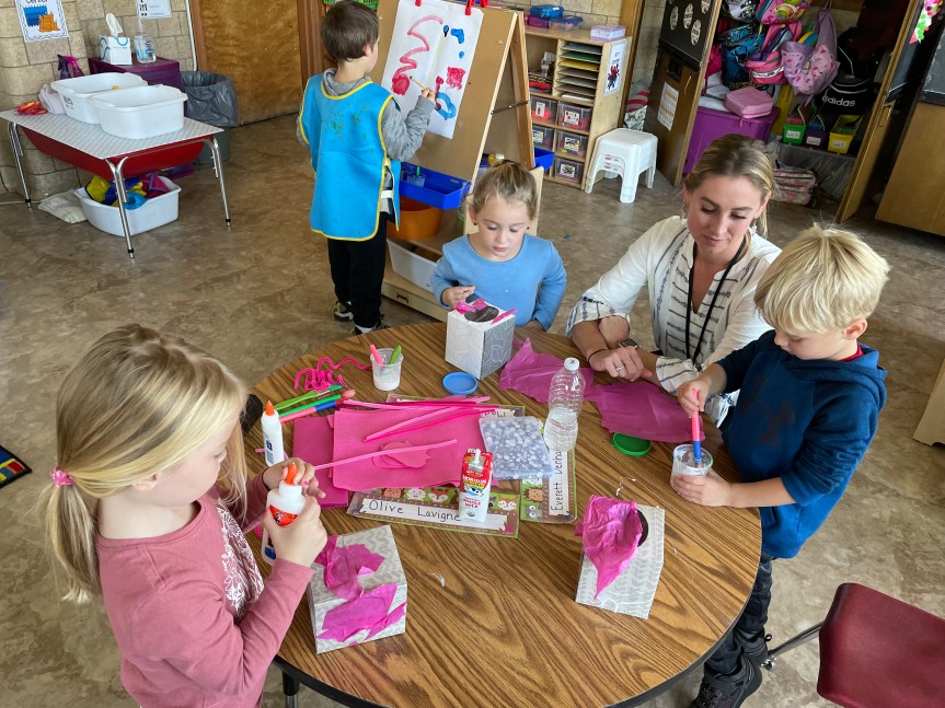 Education Technician, Erin Denham, supports Pre-K children as they problem solve how to attach the curly pipe cleaner tails to their pig pinata. 