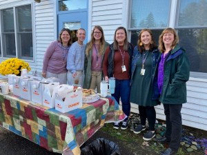teachers in a group picture with coffee and pastries on a table in front of them, outside the school