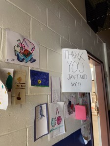 Children's artwork hanging on a wall. One extra large card reads "THANK YOU JANET"