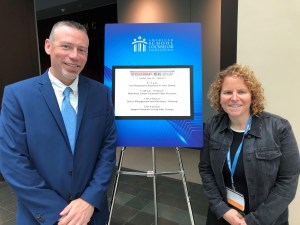 two pose for picture with conference agenda picture