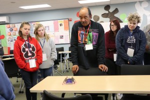 students and teacher standing looking at a robot