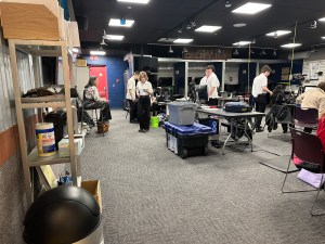 Northern Penobscot Tech Region III Instructor Laura Manzo sitting on a stool helping students who are competing in the TV/Video Production competition.