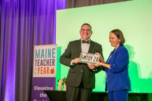 Secretary of State Shenna Bellows presenting a specialty license plate to 2024 Teacher of the Year Joshua Chard.