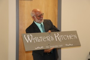 Walter Beesley holds up the new kitchen sign dedicating the space to him for his efforts to launch the classroom.