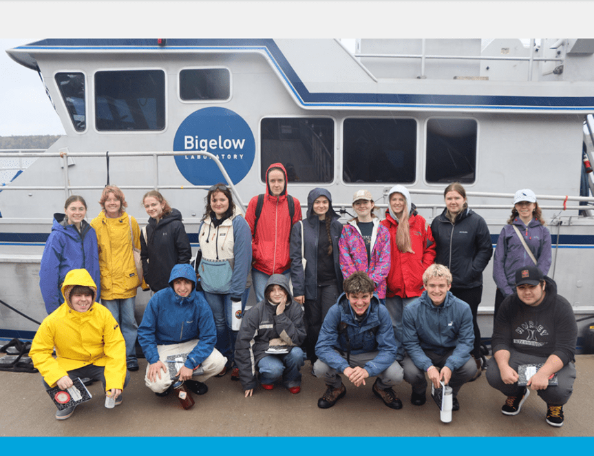 group of students posing next to a boat