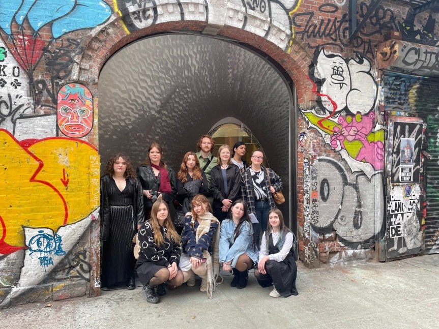 Students sitting in group picture on street in NYC in arch with artistic graffiti on brick walls